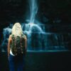shallow focus photography of woman with backpack in front of water falls