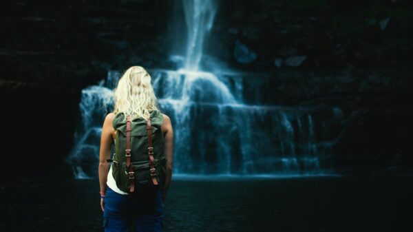 shallow focus photography of woman with backpack in front of water falls